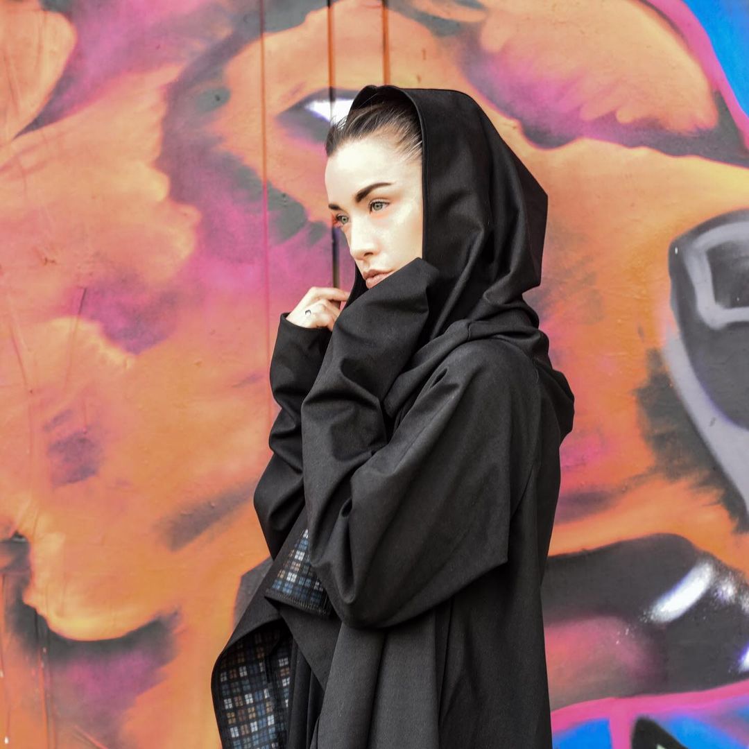Hooded cape jacket against a pink graffiti wall